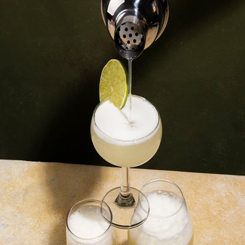 Coctel Pisco Sour peruano con rodaja de limon y shaker